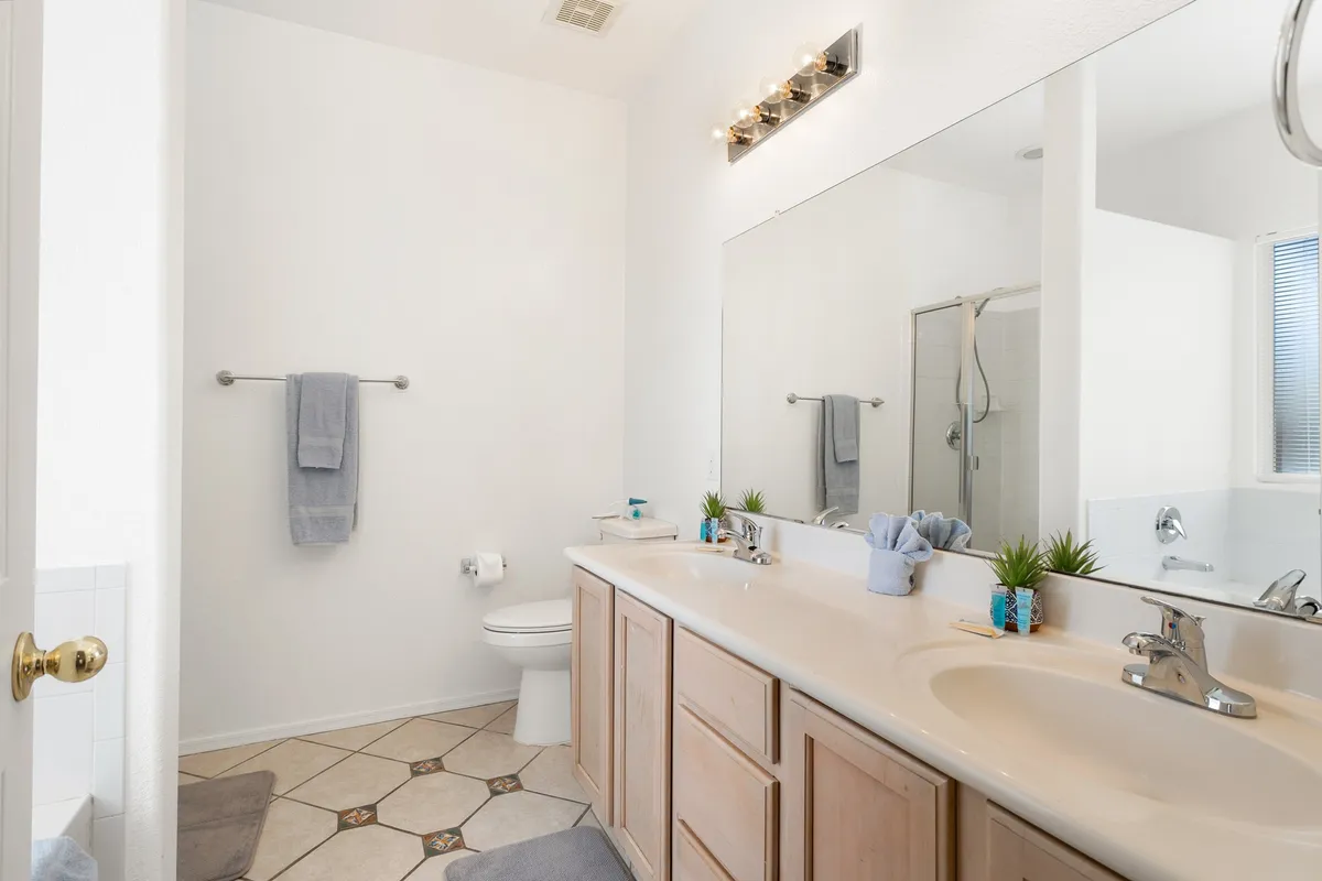 A modern, spacious bathroom with a double vanity sink, large mirror, and sleek shower area. The layout is bright, organized, and evokes a spa-like atmosphere. Subtle decorative touches and soft lighting contribute to an environment dedicated to self-care and relaxation.