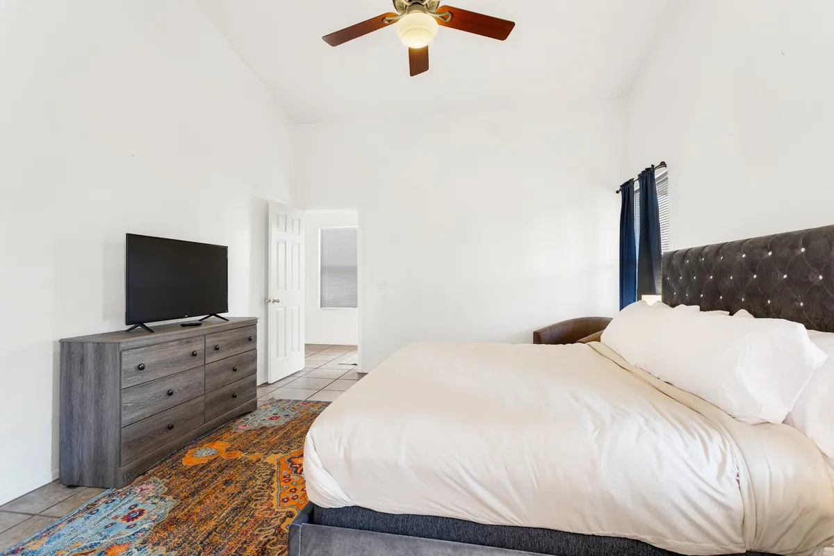 A serene bedroom with a cozy bed, soft rug, and large windows allowing in gentle daylight. The room is equipped with a television and is stylishly furnished, inviting guests to unwind, read, or enjoy a quiet movie night.