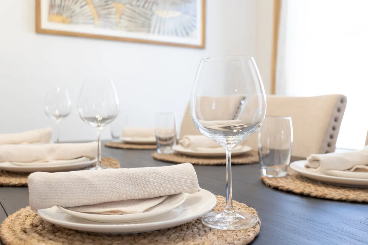 A warmly lit dining table set for a meal, with wine glasses, plate settings, and woven placemats. The surrounding environment is inviting, suggesting opportunities for indoor-outdoor transitions and gatherings.