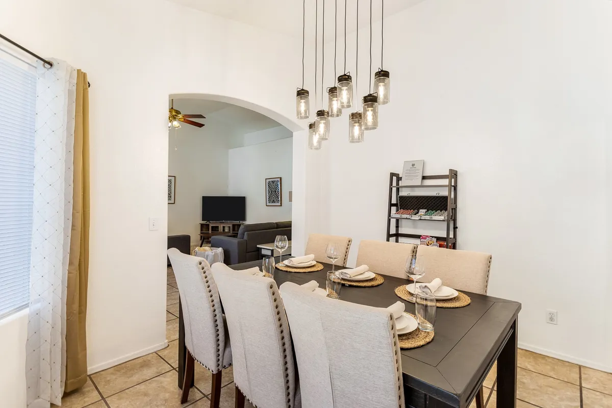 A welcoming dining area featuring a large table, stylish hanging light fixtures, and an arched entryway. The setup invites group gatherings, shared meals, and social activities.