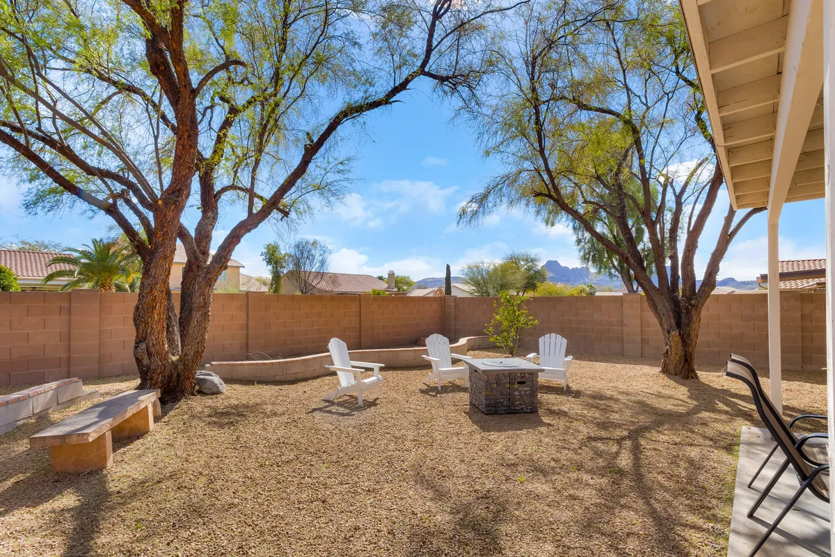 A cozy backyard scene featuring a fire pit surrounded by Adirondack chairs and a wooden bench, all nestled under mature trees. The space invites relaxation and social gatherings, with the fire pit as a central focal point for stargazing or enjoying cool evenings.