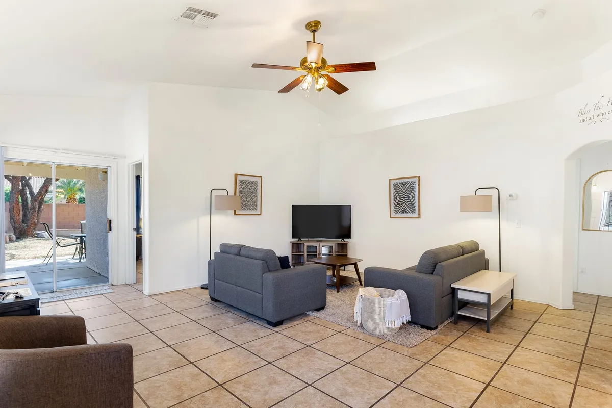 A spacious, cozy living room with ample plush sofas, a large television, decorative artwork on the walls, and a ceiling fan above. The seating is arranged for socializing or watching TV, and the overall vibe is inviting and perfect for family gatherings or relaxed evenings.
