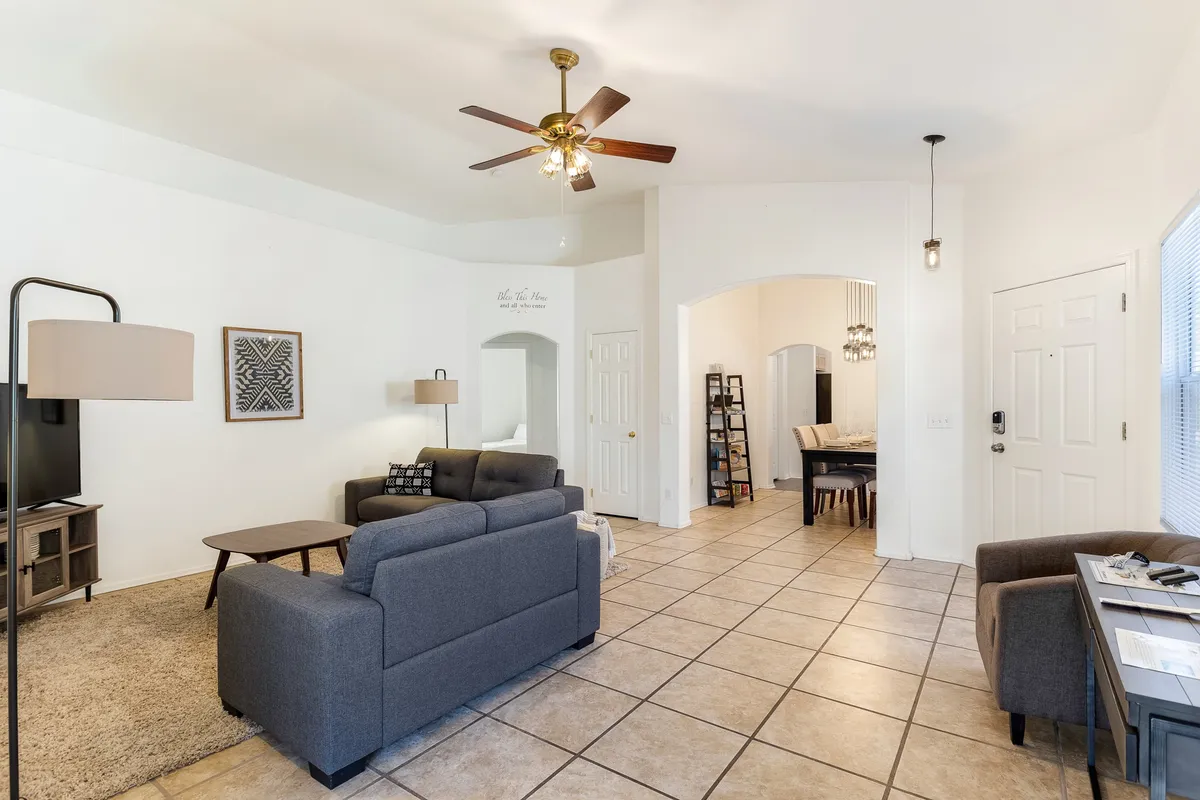 A wide-angle view of a comfy living room with a sofa set, a well-equipped entertainment center with TV, and a dining area visible in the background. The open layout seamlessly connects lounging and dining spaces, ideal for both relaxation and family interactions.