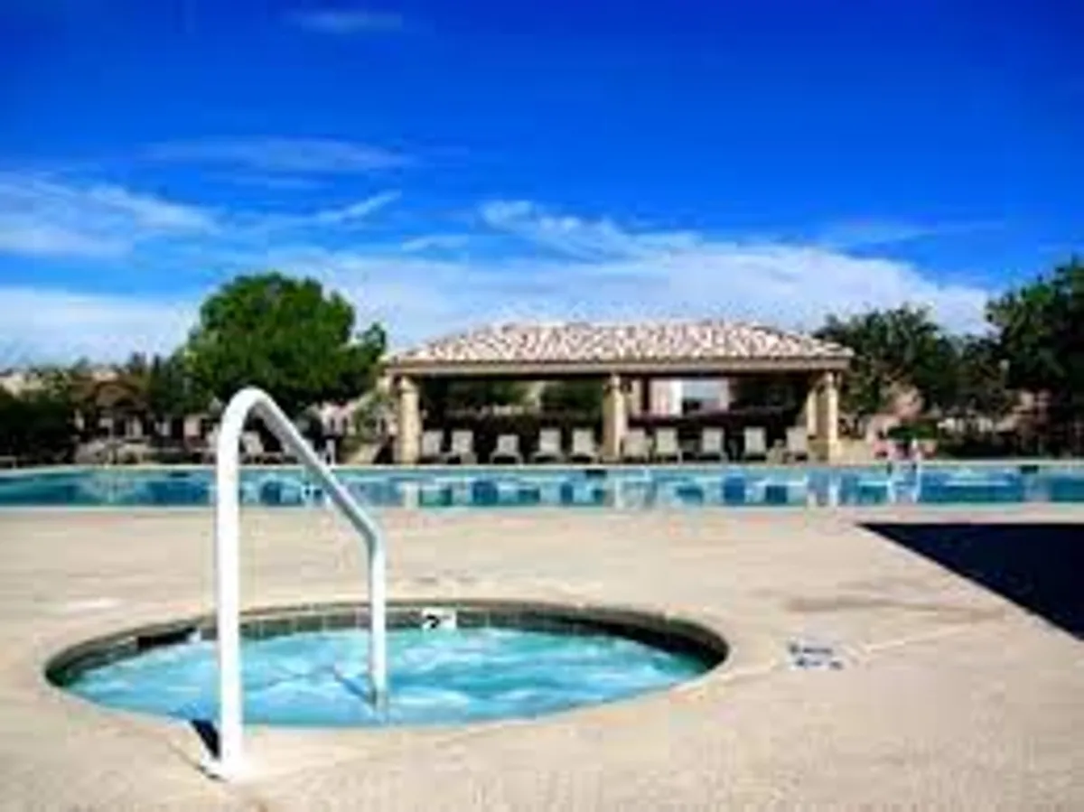 A vibrant outdoor scene centered on a sparkling swimming pool surrounded by a jacuzzi and a covered gazebo. The pool area is inviting, with ample space for both relaxation and playful activities, and the lighting suggests a pleasant time of day for family enjoyment.