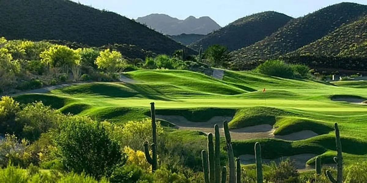 A lush, green golf course stretches across rolling hills, dotted with iconic saguaro cacti and framed by distant mountain peaks. The fairway glows in the golden hour light, hinting at the tranquility and natural beauty of Arizona. Occasional wildlife, like birds and rabbits, can be spotted along the manicured grass, capturing the essence of outdoor recreation.
